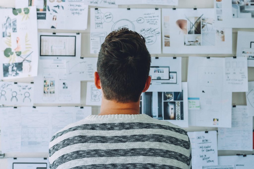 southeast asian man from behind, looking at board full of papers and ideas.